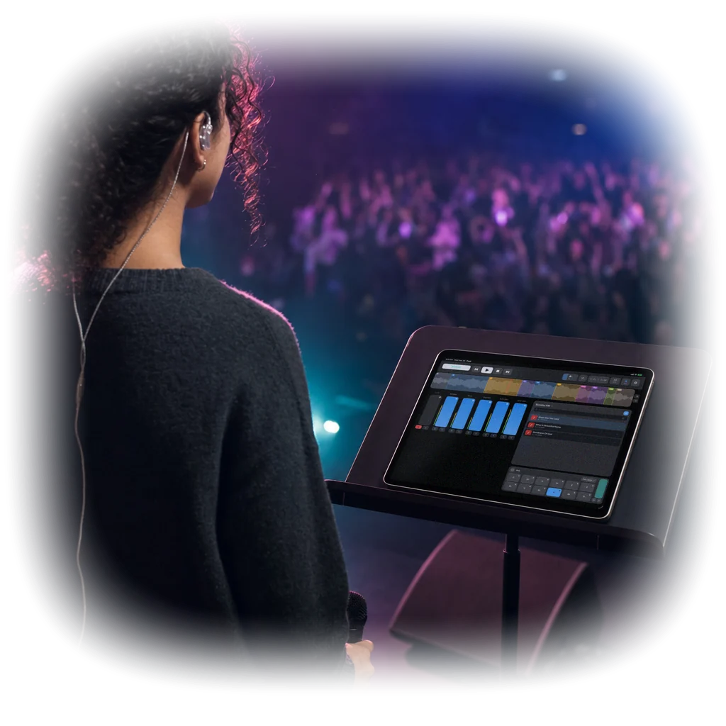 Over-the-shoulder photo of a worship leader with in-ear monitors and a microphone on stage, reading PeakMultitrack’s mixer and setlist on an iPad on her music stand, facing the crowd